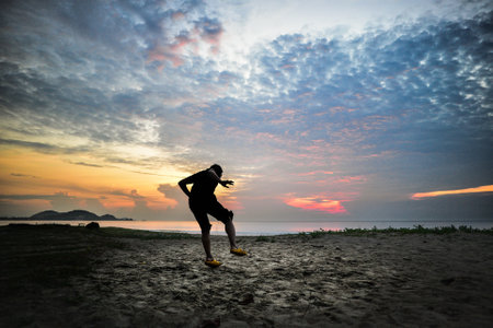 A man jumping in a sand beach at the evening with a body of water and colorful sky in the background