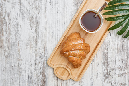 A top view shot of a croissant and a coffee on a wooden boardの写真素材