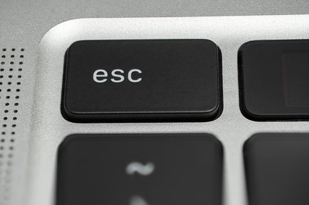 Macro shot of an Esc (escape) button on a black laptop keyboard with a silver metallic background.の写真素材