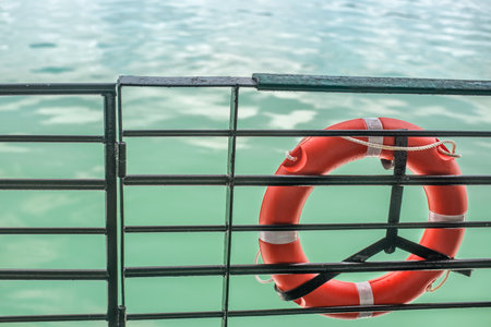 A closeup shot of a red lifebelt tied up on a metal fence against a body of water