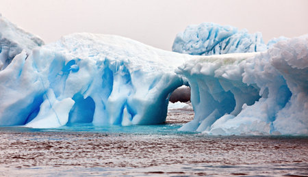 A photo of a blue iceberg with a big arch in a cold water with few icebergs in the background...