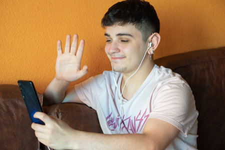 young man making a video call and waving to his smart phone sitting on a sofa. distancing concept....