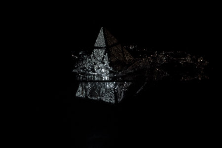A closeup of a small pyramid figure falling into the water isolated on a black backgroun