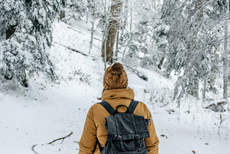A rearview of a girl hiking on a path in the woods. Adventure in winter forest