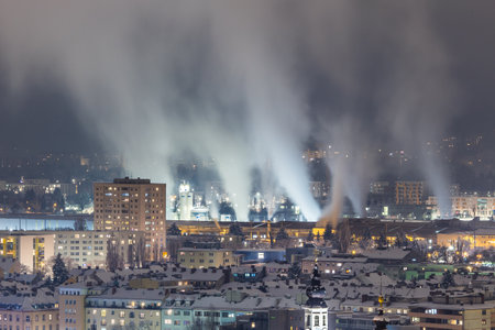 Night city view with buildings and a smoking industrial steel mill with impressive exhaust gasesの写真素材