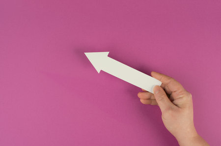 Holding an arrow in the hand, symbol for growth, success and development, pink colored background, copy space for textの写真素材