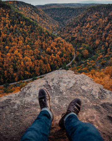A male feet sitting on the rock against forest mountains with bright green and orange autumn treesの写真素材