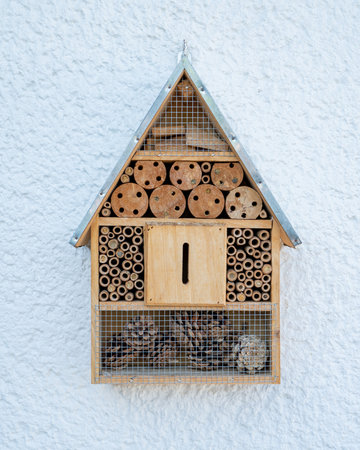 A wooden insect house hanged on a white wall.