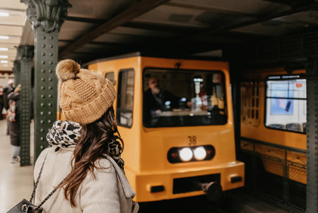 Rear view of woman wearing stylish winter clothes, waiting for yellow train at metro station on line one in Budapest, Hunagry.の写真素材