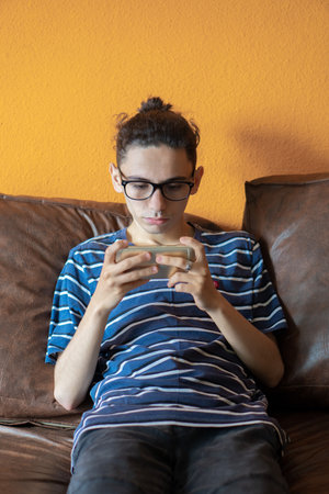 young caucasian man playing video games on his smart phone sitting on the sofa