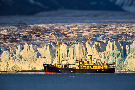 A yellow industrial ship against a massive glacier in Svalbard, Norwayの写真素材