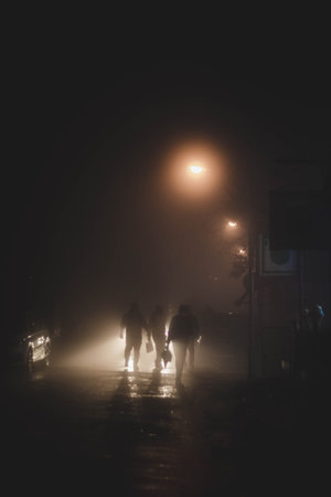 A vertical shot of people walking down the street with street lights covered in the fog at nightの写真素材