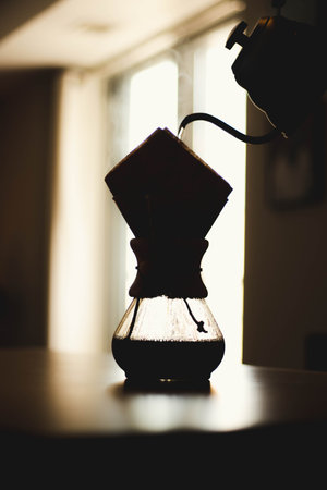 A vertical closeup shot of the pour over coffee maker in the morning on the blurry background