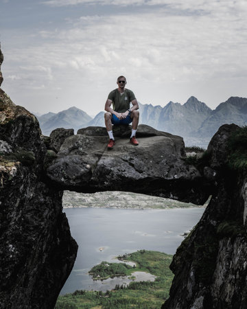 A Caucasian hiker sitting on a rock between two cliffs with the view on the cloudy sky, hills and seaの写真素材