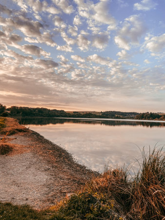 A vertical shot of a lake with reflecting trees against a blue sky with clouds in the sunsetの写真素材