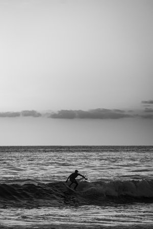 A vertical of a person surfing on a board in sea waves shot in grayscale