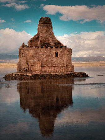 A vertical shot of an ancient stone building in the middle of a lake against blue sky
