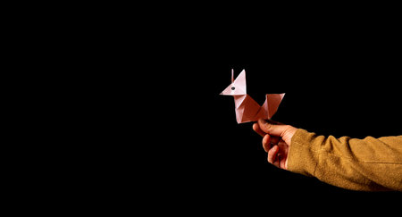 A closeup shot of the male hand holding origami paper fox on the black backgroundの写真素材