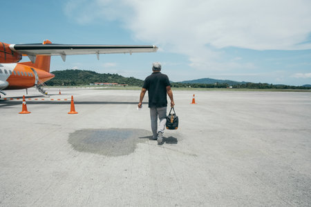 An old man with a bag walks down the runway to his orange planeの写真素材