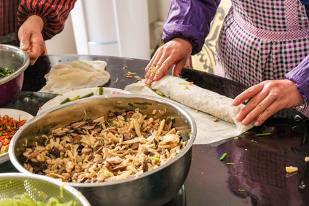 A closeup of a chef spreading a dough next to a metal pot of Rumali shawarma on a reflecting surfaceの写真素材