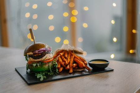 A tasty burger served with fries and sauce. Fast food in the background with bokeh lightsの写真素材