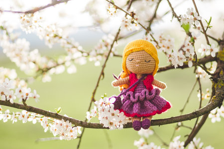 A product photo of a handmade crochet doll on a branch of cherry blossom treeの写真素材