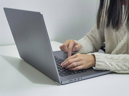 A woman in a white sweater working on a gray laptop on a white table