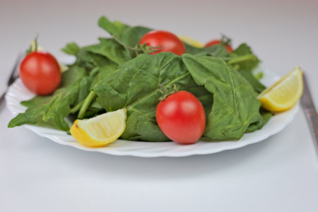 A closeup of a salad made from lemons, cherry tomatoes and spinach on a white plate