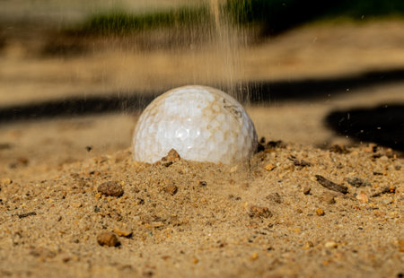 A closeup of a golf ball stuck in the sand
