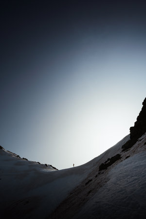 A vertical photo of a person hiking on snow-covered mountains