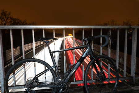 A long exposure shot of a bicycle parked against a metal fence over a  highway with the lights of cars at nightの写真素材