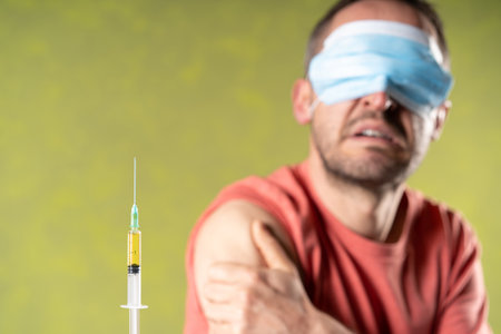 Burred Suspicious man looks doubtfully  a focused close-up  syringe with anti covid vaccine in a green background.の写真素材