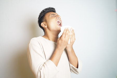 A young man sneezing with his mouth open holding a napkinの写真素材