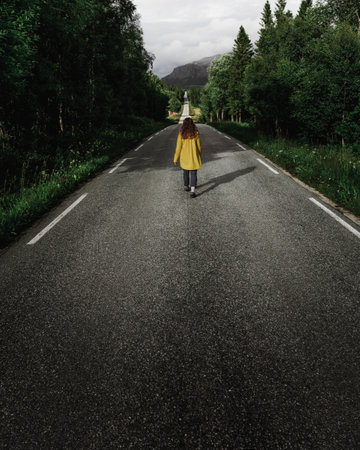 A vertical shot of a woman walking by the asphalt road - concept of reaching targets, aimsの写真素材