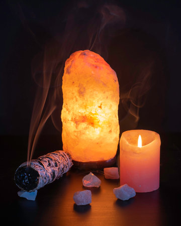 A vertical shot of the burning sage with candle and crystals in the dark