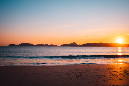 A sunset over a sandy beach surrounded by mountains