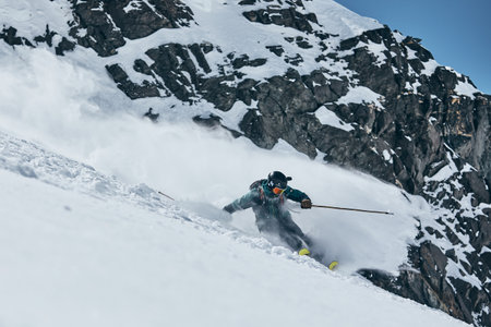 A skier slides in the high mountains with snowy hills on the background