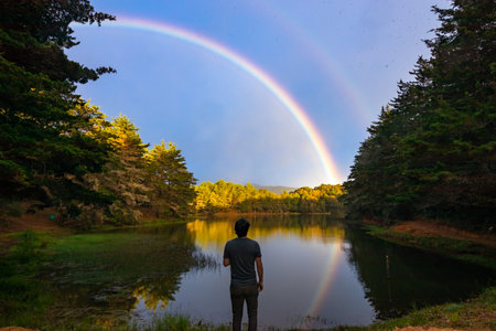 A man standing by the lake and looks at the rainbowの写真素材