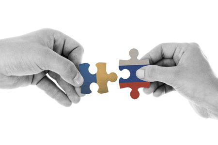 Two hands holding puzzle pieces with the flags of Ukraine and Russia indicating the conflict