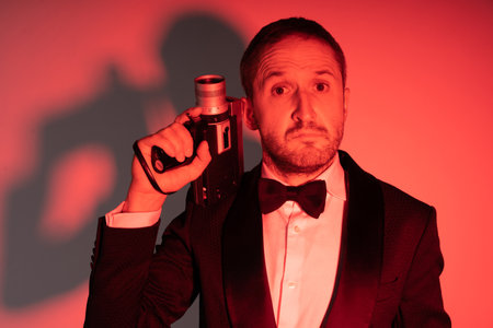 Man in an elegant suit handling a Super 8 camera in classic secret agent pose. Red light...