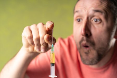 A burred man touches doubtfully  the focused close-up  syringe needle with anti covid vaccine in a...