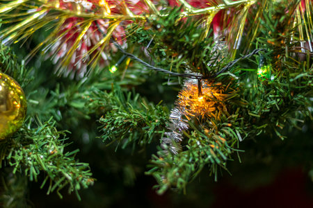 Green branches of a festive Christmas tree decorated with glitter tinsel and a garland.の写真素材