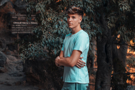 A young blonde Spanish man standing in the park with crossed handsの写真素材