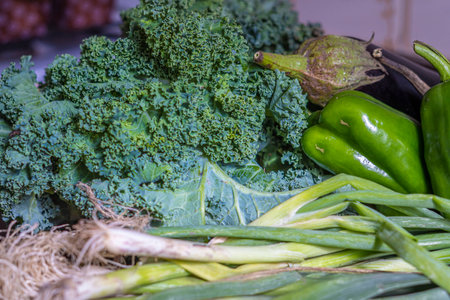 A closeup shot of organic green peppers, kale, and onions