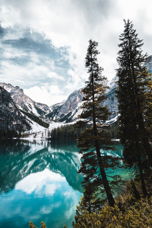 A Beautiful scene of fir trees by reflecting water lake against snowy mountains and a gray light skyの写真素材