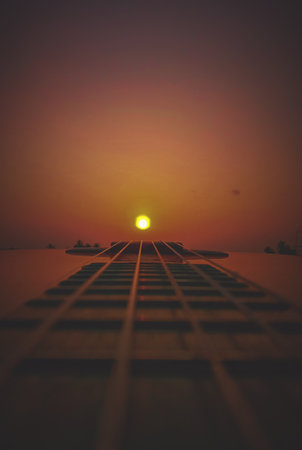 A vertical shot of guitar strings with golden sunset backgroundの写真素材