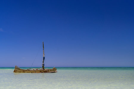 A beautiful view of a small sailing boat on the shallow seawater against a sunny blue horizon skyの写真素材