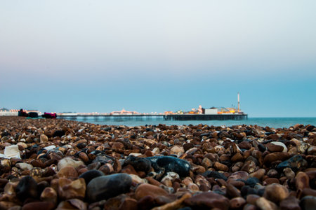 A closeup of stone beach on the sea with a view of pier under the blue sky