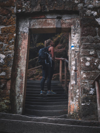 A vertical shot of a female backpacker standing on the stairs under an old stone archの写真素材