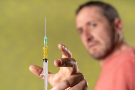 A blurred man tries to grab with his hand a focused close-up  syringe with anti covid vaccine in a green background.の写真素材